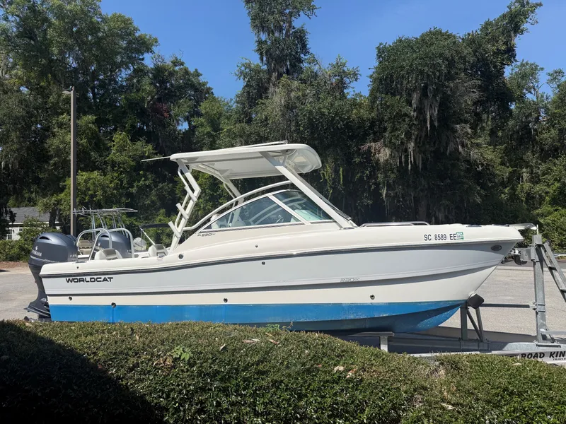 Slide: The Image of A white 2023 World Cat 230 DC boat on a trailer, surrounded by trees. - 12