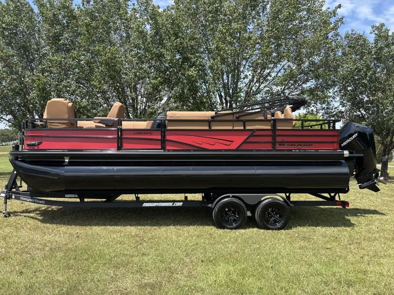 The Image of A red 2026 Ranger Fish and Cruise Series 223FC pontoon boat on a trailer in a grassy area. - 1