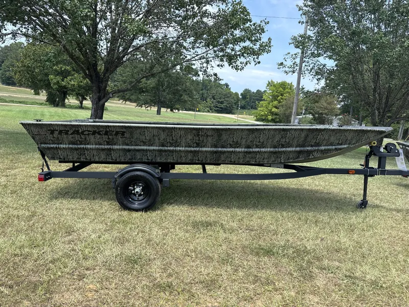 The Image of The image shows a Tracker Grizzly 1648 Utility boat on a trailer, surrounded by trees and grass. - 1