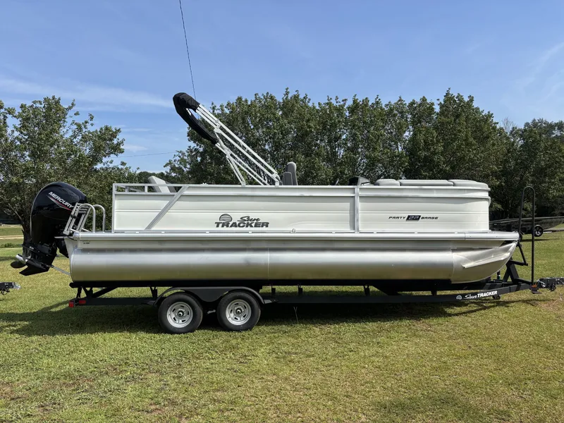 The Image of A Sun Tracker Party Barge 22 RF DLX pontoon boat on a trailer on a grassy field. - 1