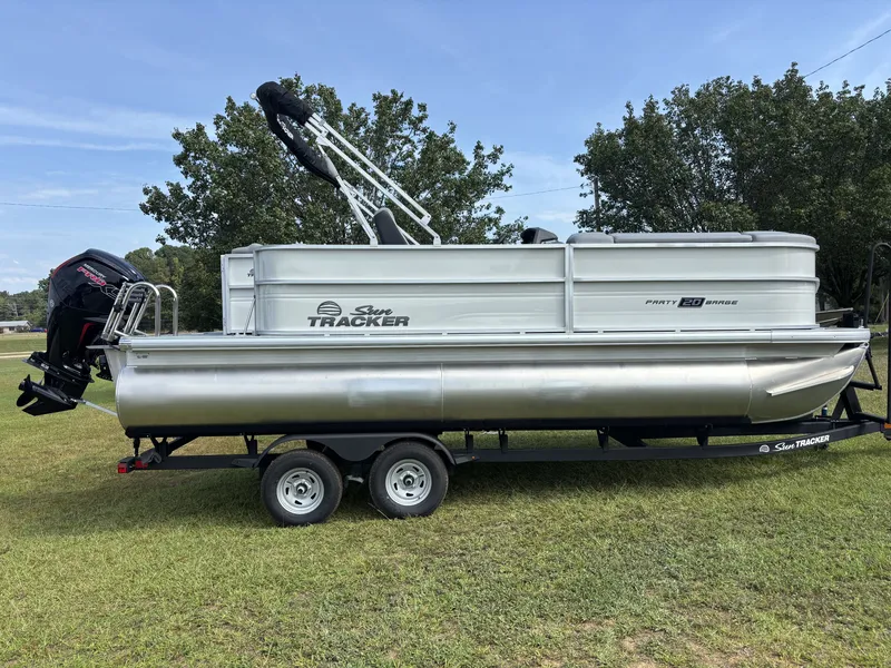 The Image of A 2026 Sun Tracker Party Barge 20 DLX pontoon boat on a trailer on grass. - 1