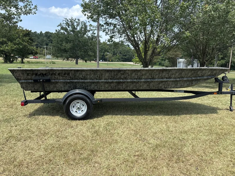 The Image of A 2026 Tracker 1860 Utility boat on a trailer, set on grass, surrounded by trees. - 1