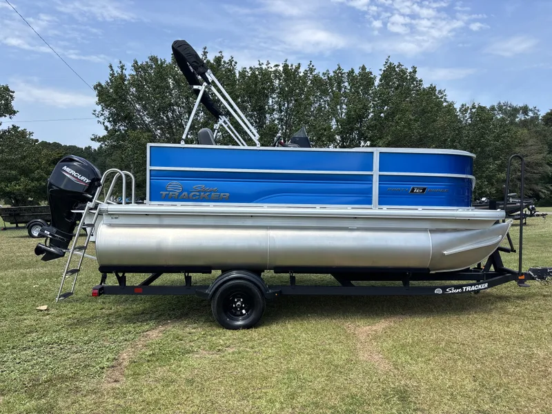 The Image of A blue Sun Tracker Party Barge 16 DLX pontoon boat from 2027 sits on a trailer on grass. - 1