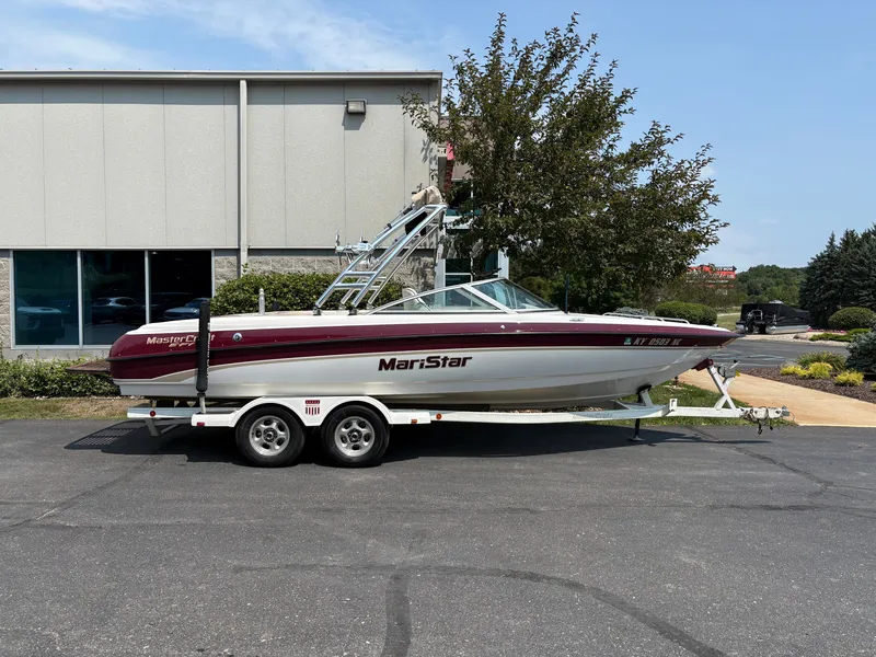 The Image of A 2000 MasterCraft 230 VRS boat on a trailer parked in front of a building. - 1