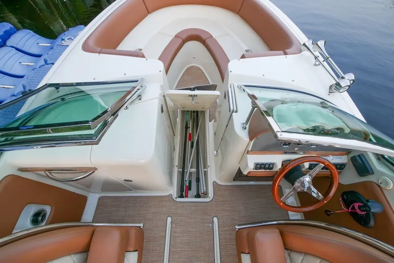 Slide: The Image of 2018 Chris-Craft Launch 27 boat interior with open storage, brown seating, and wooden steering wheel. - 26