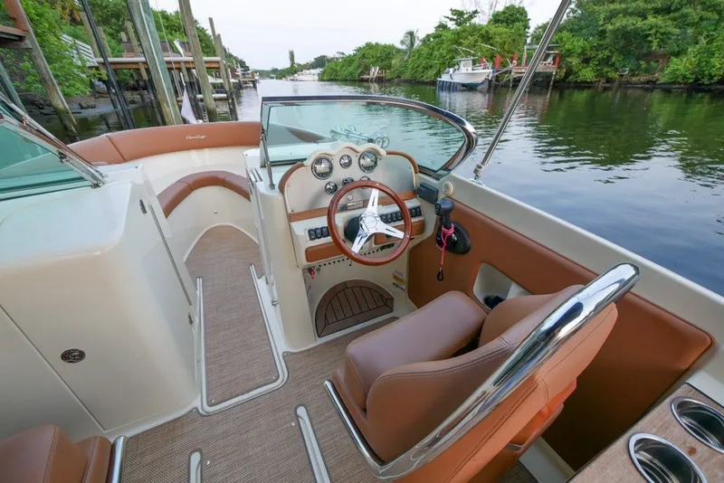 Slide: The Image of 2018 Chris-Craft Launch 27 boat interior with steering wheel and dashboard, docked by a scenic river. - 20