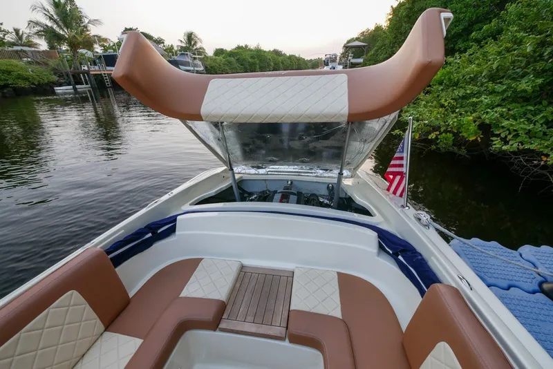 Slide: The Image of 2018 Chris-Craft Launch 27 boat interior with tan and white seating, docked by lush greenery. - 12