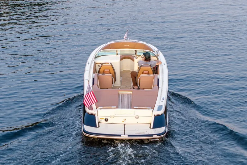 Slide: The Image of 2018 Chris-Craft Launch 27 boat cruising on calm water, rear view with American flag. - 2