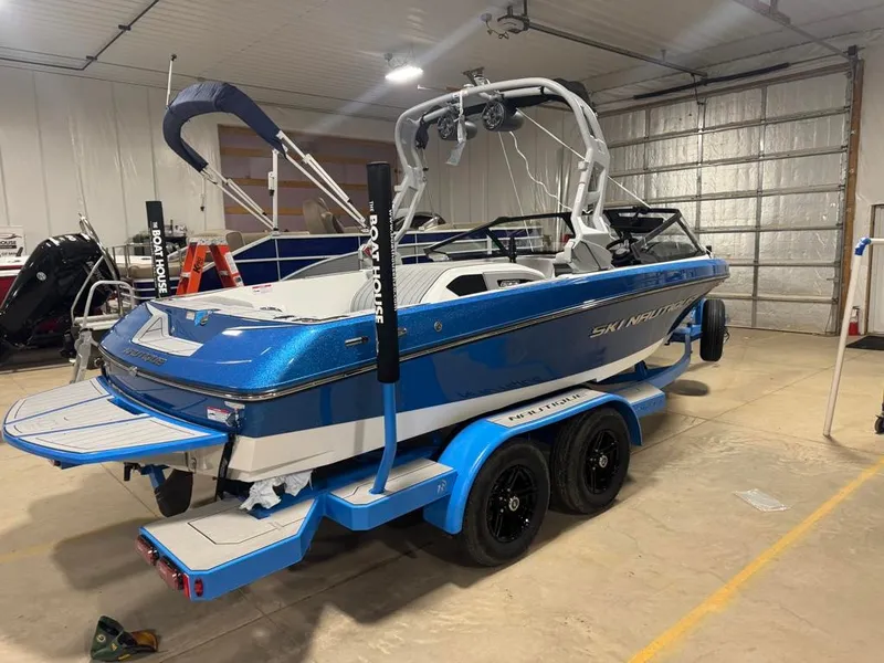 Slide: The Image of A blue 2025 Ski Nautique 200 Open Bow sits on a trailer in a warehouse. - 9