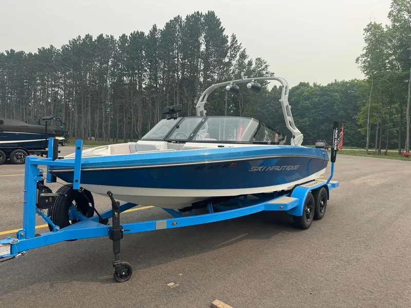 Slide: The Image of A blue and white 2025 Ski Nautique 200 Open Bow on a blue trailer in a wooded area. - 4