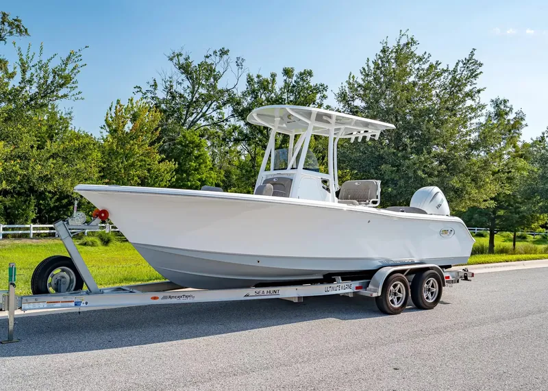 The Image of A 2027 Sea Hunt Ultra 229 boat on a trailer, surrounded by trees and clear skies. - 1
