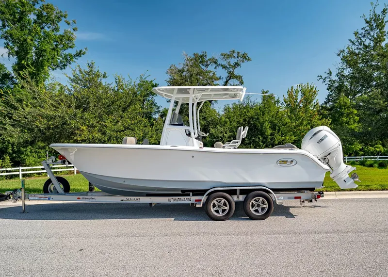 Slide: The Image of A 2027 Sea Hunt Ultra 229 boat on a trailer, surrounded by trees. - 2