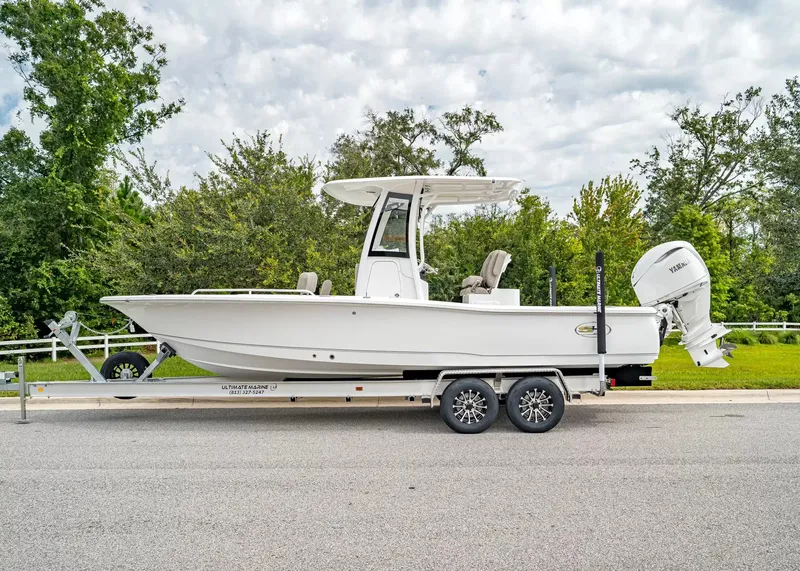 Slide: The Image of A white 2027 Sea Hunt BX25FS boat on a trailer, surrounded by trees. - 2