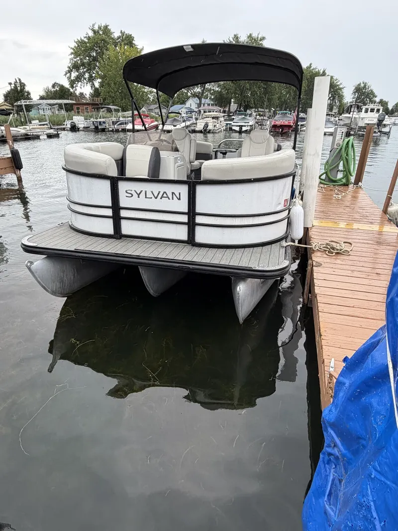 Slide: The Image of A 2023 Sylvan Mirage X X1 pontoon boat docked at a wooden pier in a calm harbor. - 2