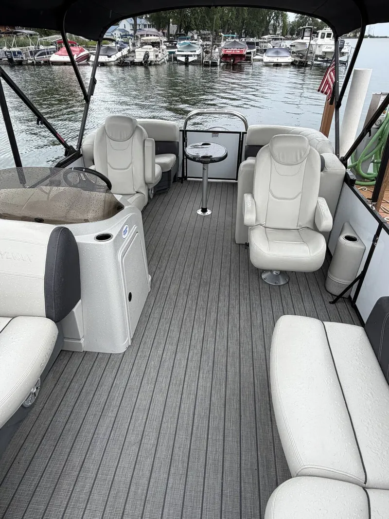 Slide: The Image of The image shows the interior of a 2023 Sylvan Mirage X X1 pontoon boat with gray flooring and beige seating. - 3