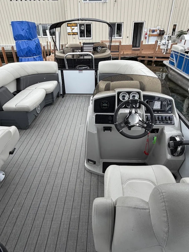 Slide: The Image of The image shows the interior of a 2023 Sylvan Mirage X X1 pontoon boat with gray flooring and comfortable seating. - 4