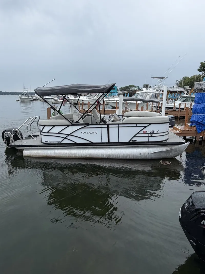 The Image of A 2023 Sylvan Mirage X X1 pontoon boat docked. It features a black canopy. - 1