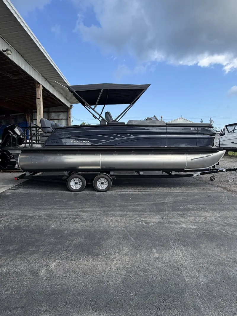 The Image of A 2027 Sylvan L3 RLZ Platinum pontoon boat sits on a trailer under a covered area. - 1