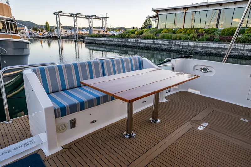 Slide: The Image of Luxury deck seating on 2023 North Pacific 53 Euro yacht, featuring striped cushions and wooden table. - 70