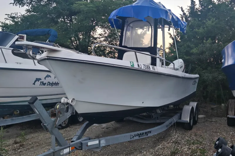 Slide: The Image of 2015 May-Craft 2300 CCX boat on trailer, parked outdoors with trees in background. - 18