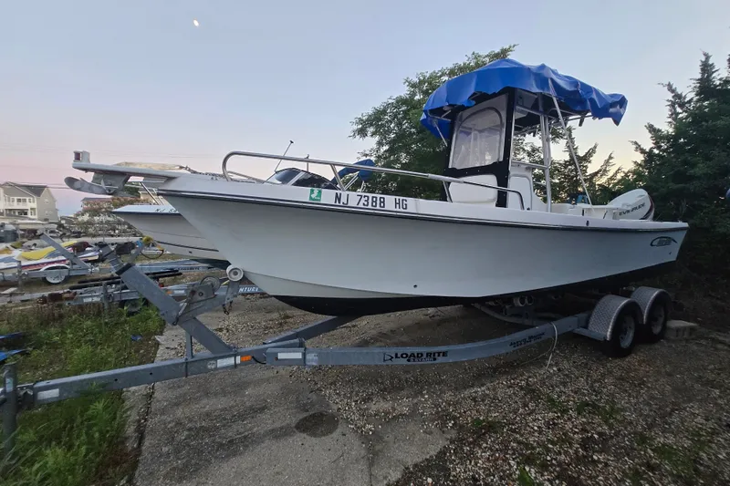 The Image of 2015 May-Craft 2300 CCX boat on trailer with blue canopy, parked outdoors. - 0