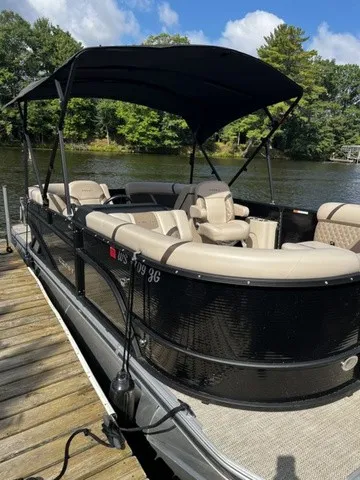 The Image of A sleek pontoon boat with a black hull and beige interior, docked on a calm river. - 2