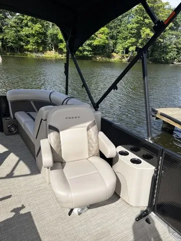 Slide: The Image of A modern pontoon boat seat with gray upholstery and cup holders, surrounded by water and trees. - 13