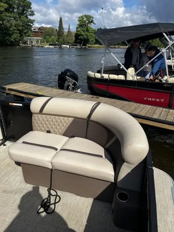 Slide: The Image of A sleek pontoon boat with beige upholstered seating, docked on a calm lake with trees in the background. - 4