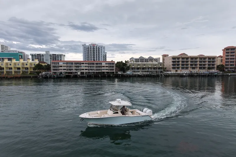 Slide: The Image of 2021 Grady-White Canyon 326 boat cruising near waterfront buildings under cloudy sky. - 14
