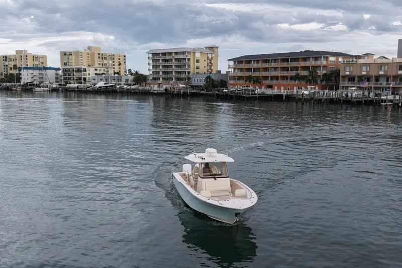 Slide: The Image of 2021 Grady-White Canyon 326 boat cruising near waterfront buildings under cloudy sky. - 32