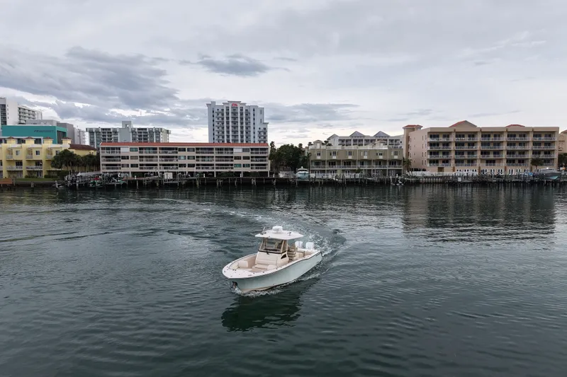 Slide: The Image of 2021 Grady-White Canyon 326 boat cruising near waterfront buildings under cloudy sky. - 17