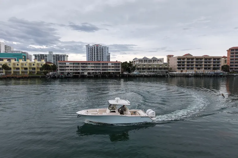 Slide: The Image of 2021 Grady-White Canyon 326 boat cruising near waterfront buildings under cloudy sky. - 15