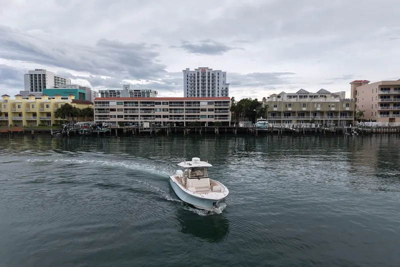 Slide: The Image of 2021 Grady-White Canyon 326 boat cruising near waterfront buildings under cloudy sky. - 20