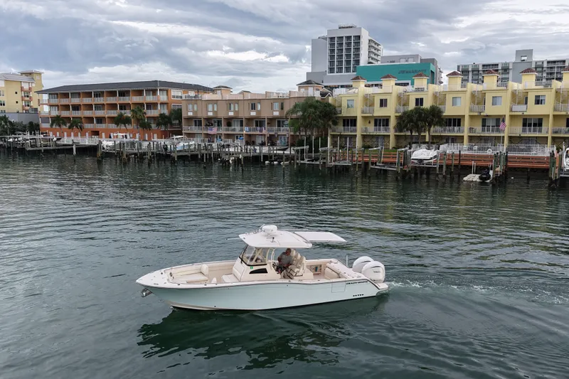 Slide: The Image of 2021 Grady-White Canyon 326 boat cruising near waterfront buildings under cloudy sky. - 21