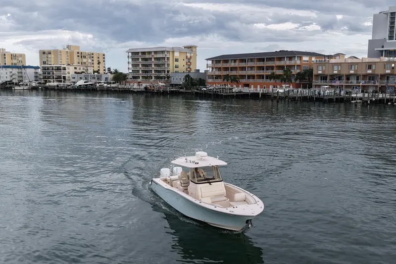 Slide: The Image of 2021 Grady-White Canyon 326 boat cruising near waterfront buildings under cloudy sky. - 29