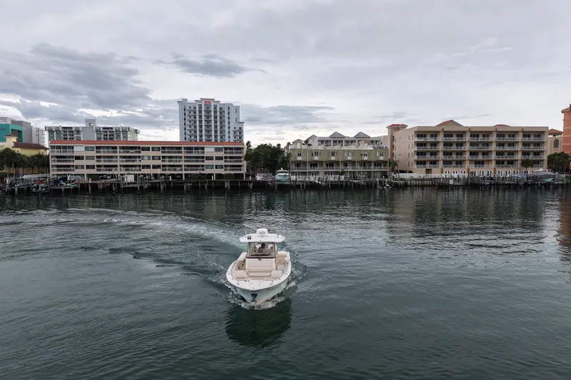 Slide: The Image of 2021 Grady-White Canyon 326 boat cruising near waterfront buildings under cloudy sky. - 18