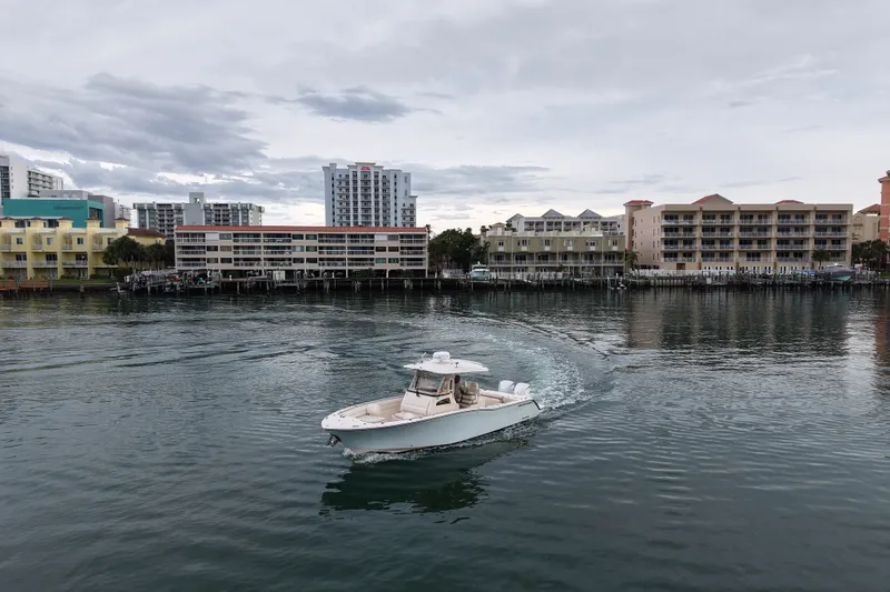 Slide: The Image of 2021 Grady-White Canyon 326 boat cruising near waterfront buildings under cloudy sky. - 16