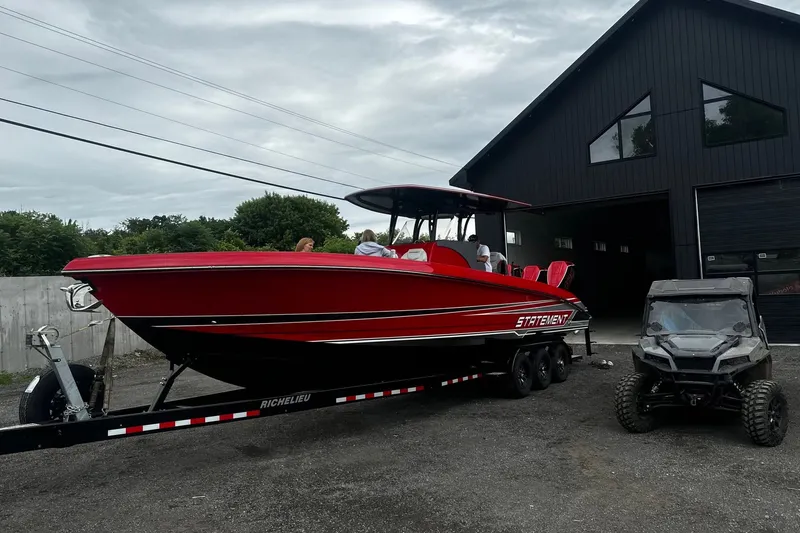 The Image of Red 2025 Statement 350 Open boat on trailer beside black building and off-road vehicle. - 0