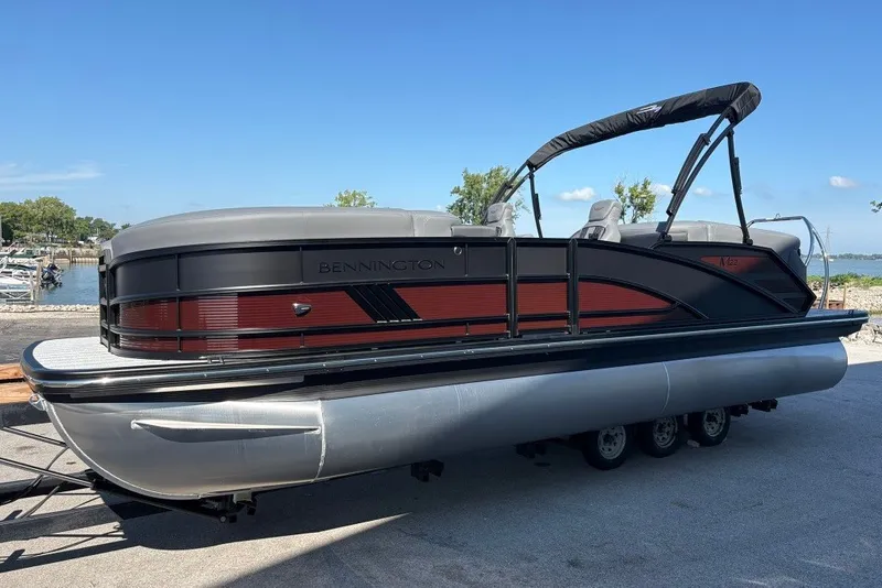 Slide: The Image of 2027 Bennington 22 M Open Fastback Quad Bench pontoon boat docked by the shore. - 2