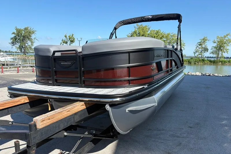 Slide: The Image of 2027 Bennington 22 M Open Fastback Quad Bench pontoon boat on trailer by a lake. - 8