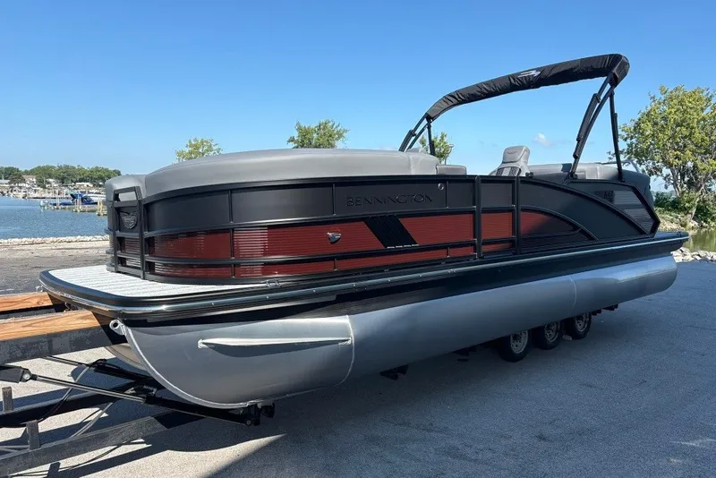 Slide: The Image of 2027 Bennington 22 M Open Fastback Quad Bench pontoon boat docked by the water. - 5