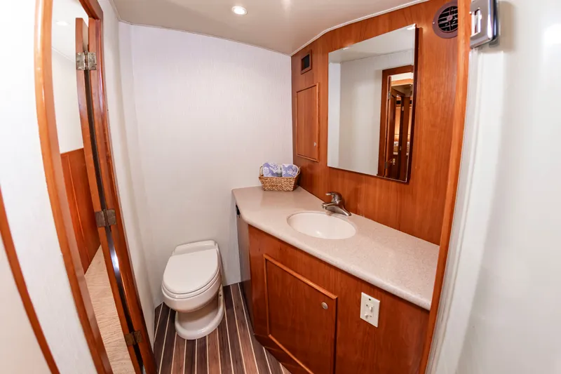 Slide: The Image of The image shows a bathroom with wooden cabinetry, a sink, and a toilet on a Custom Carolina 61' Sportfisherman boat. - 40