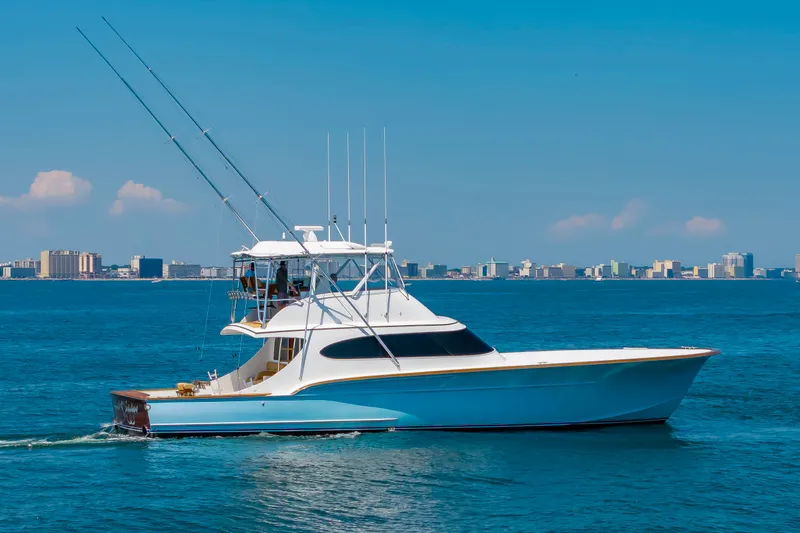The Image of A sleek white and blue sportfisherman boat cruises on calm waters with a city skyline in the background. - 1