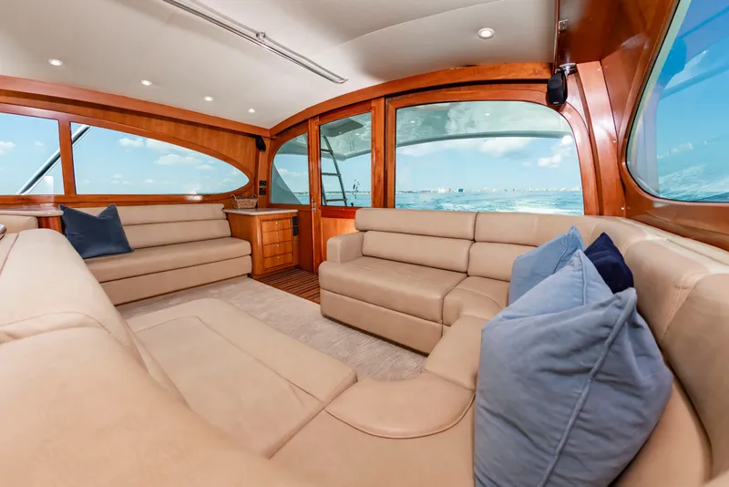 Slide: The Image of The image shows the interior of a 2004 Custom Carolina 61' Sportfisherman with beige sofas and blue pillows. - 25