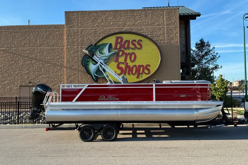 The Image of A red Sun Tracker Party Barge 22 RF DLX pontoon boat on a trailer in front of a Bass Pro Shops building. - 0