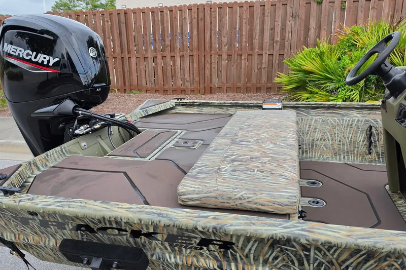 Slide: The Image of 2027 Tracker Grizzly 1860 CC boat with Mercury engine, camo design, parked outdoors. - 15