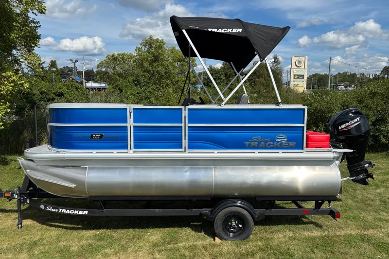 The Image of 2027 Sun Tracker Party Barge 16 DLX pontoon boat on trailer, blue and silver design. - 0