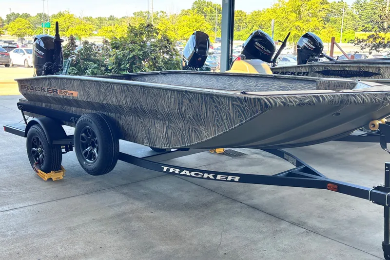 The Image of 2027 Tracker Grizzly 1756 T Marsh boat on trailer, camo design, parked outdoors. - 0