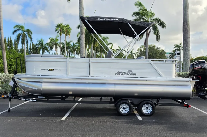 The Image of 2027 Sun Tracker Party Barge 22 RF DLX pontoon boat on trailer, parked with palm trees. - 0