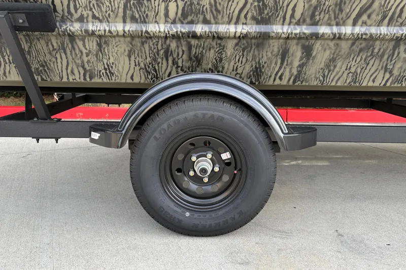 Slide: The Image of 2027 Tracker Grizzly 1754 Utility trailer wheel with camouflage design on concrete surface. - 18
